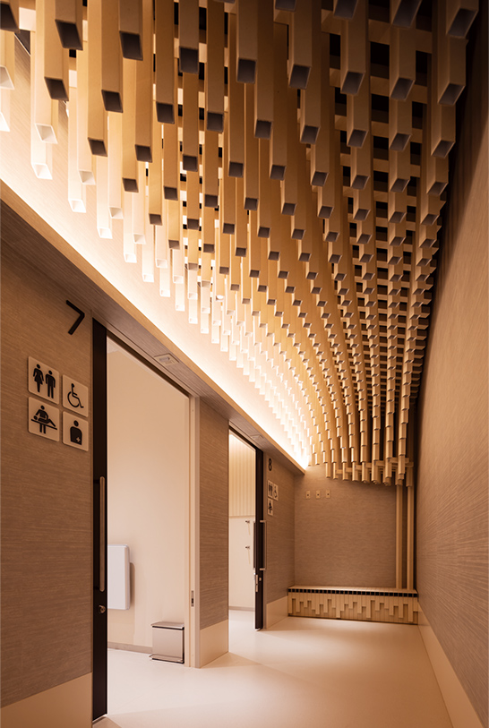 紙の筒がうねる天井 ピクトグラム 奥のピクトグラムは視認性向上のため大きい。ベンチも紙管。写真/傍島利浩